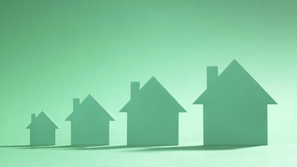 A row of four cardboard cutout houses painted green and on a green background of an increasing size.