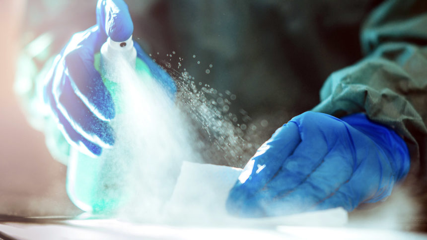 Gloved hands disinfecting a surface