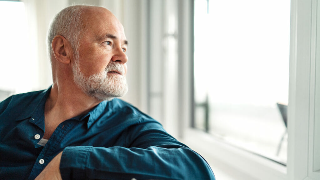 Sad old man sitting and thinking in living room.