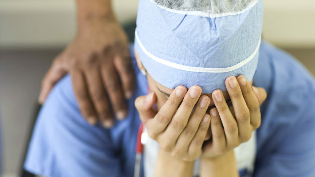 Asian surgeon sitting with head in hands